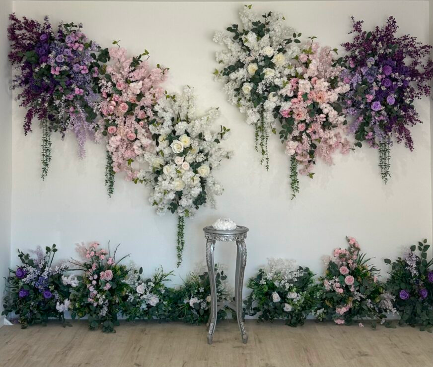 Floral arrangements on wall with pedestal centerpiece.
