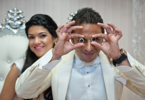 A groom holding wedding rings and the bride smiling behind him