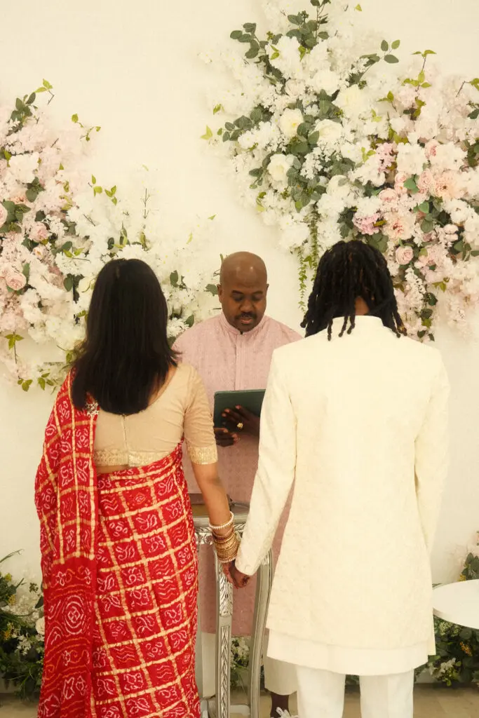 Couple at ceremony with floral backdrop.
