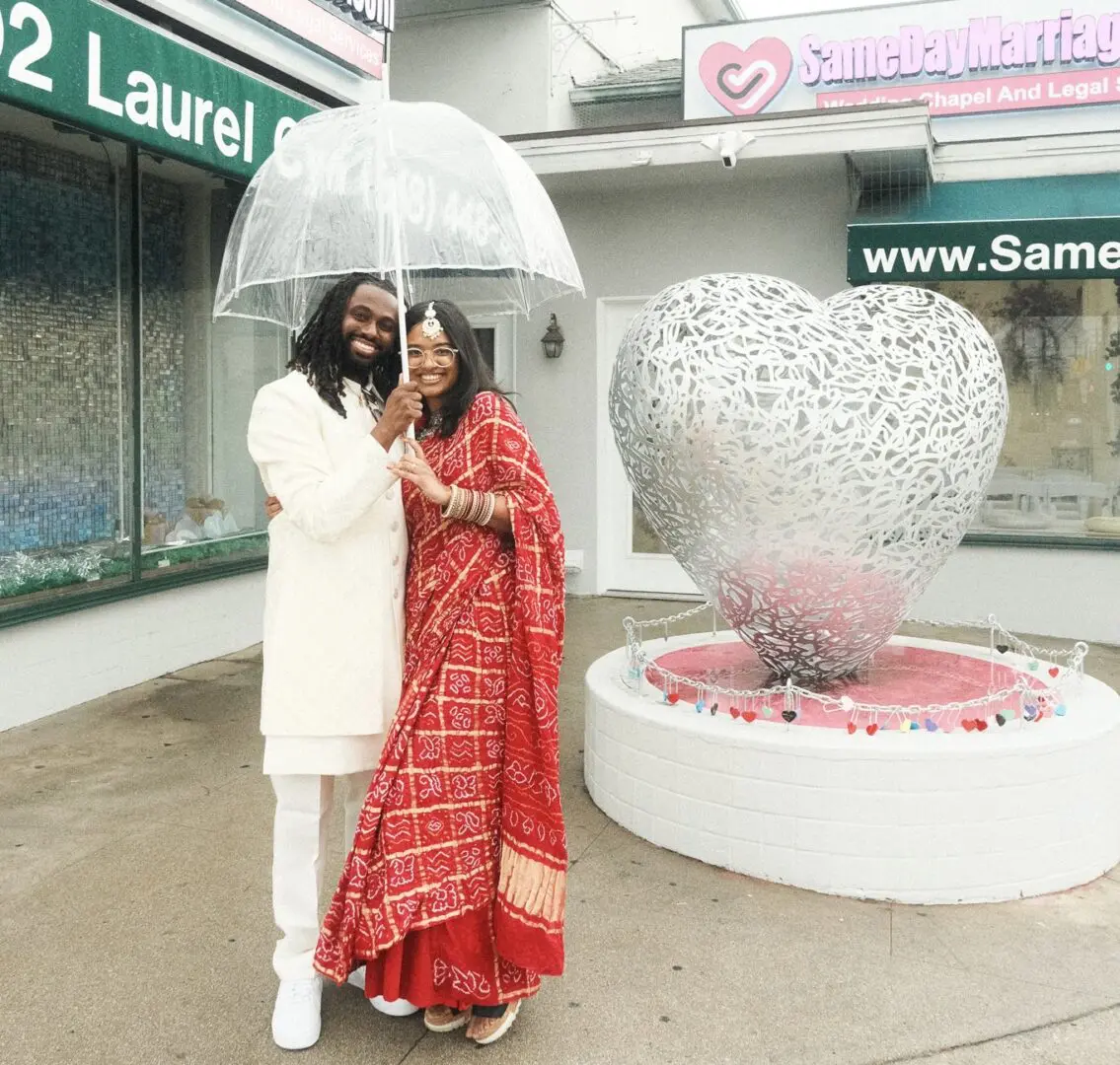 Couple under umbrella near large heart sculpture.