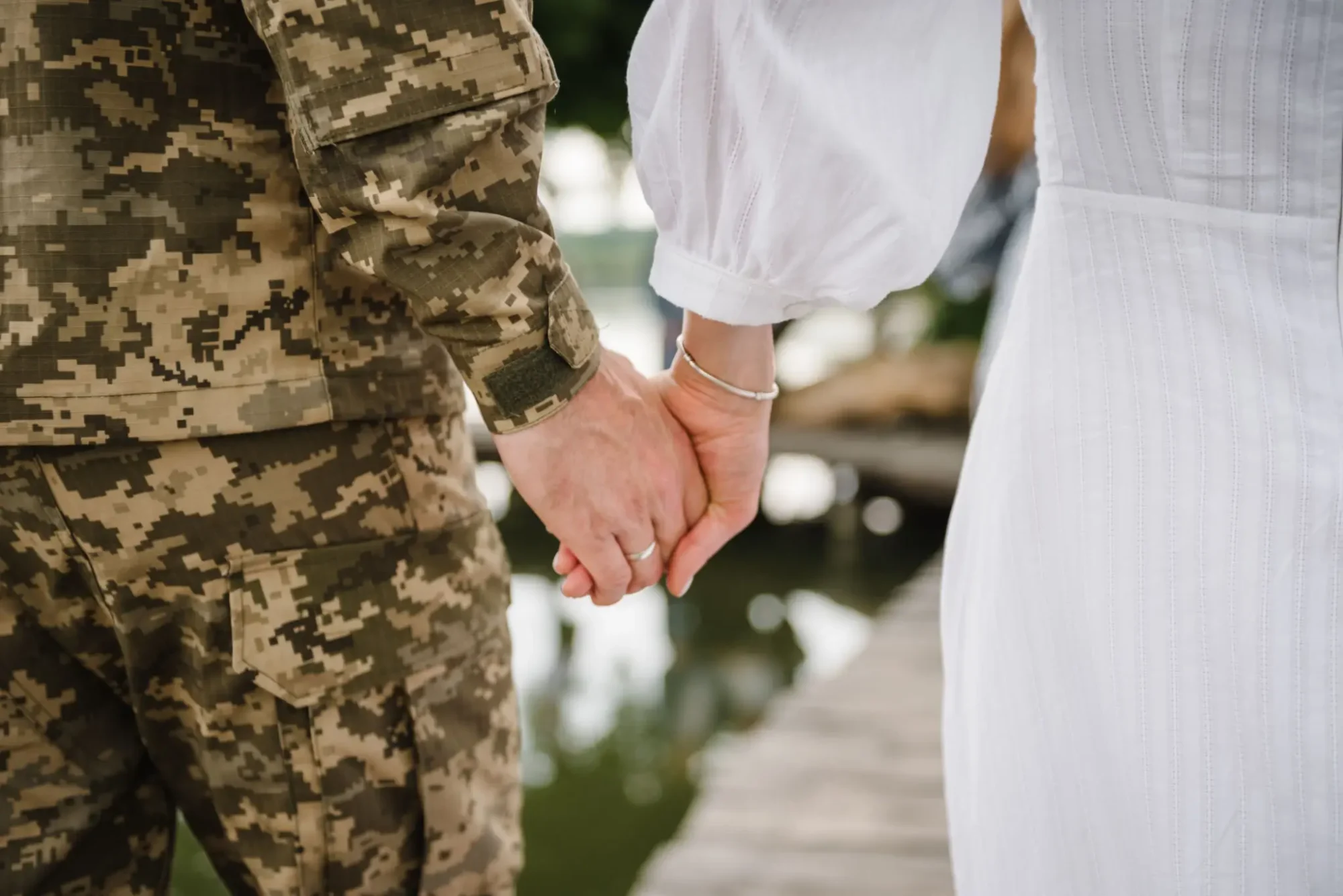 A couple holding hands, one in military uniform and the other in white clothing.