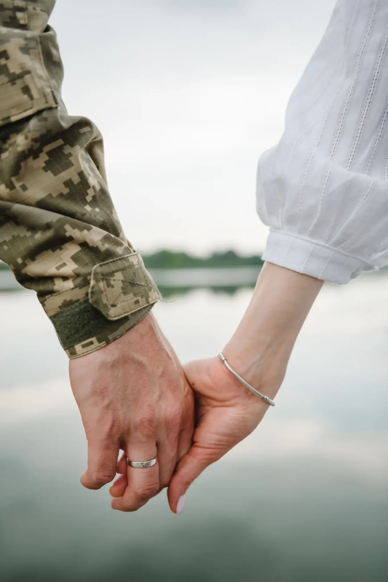 Two people holding hands, one in camouflage and the other in white.